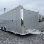 a silver stealth trailer is parked in a gravel lot
