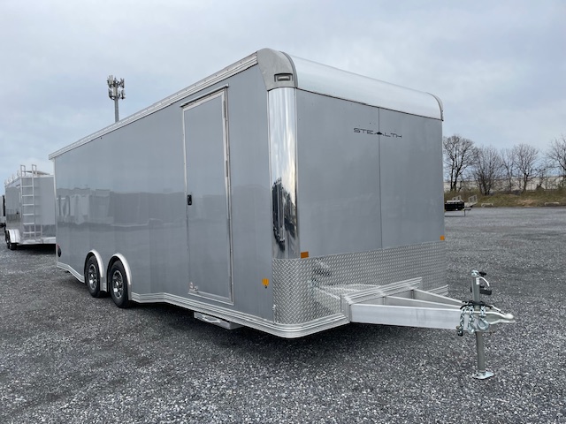 a silver stealth trailer is parked in a gravel lot